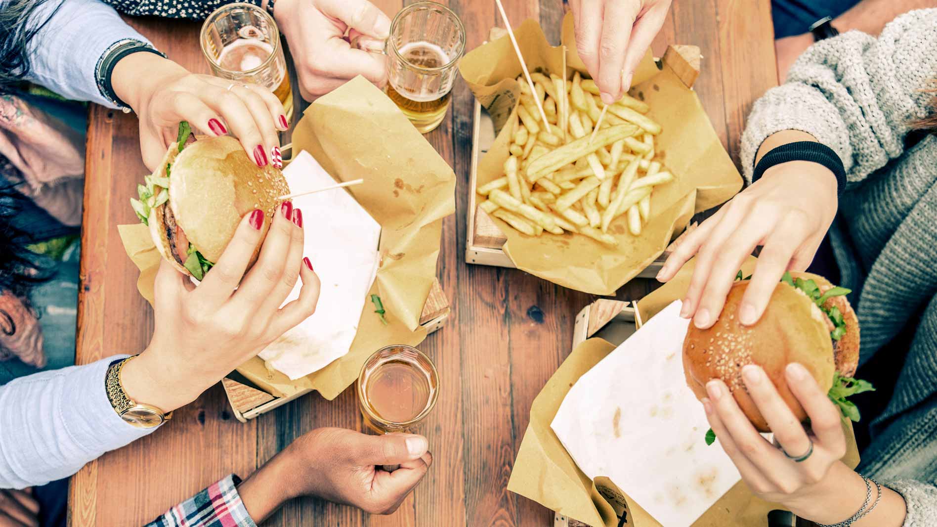 Grupo de personas compartiendo hamburguesas y papas fritas en una mesa de madera
